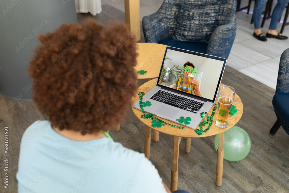 Mixed race man at bar having st patricks day video call with friend on laptop