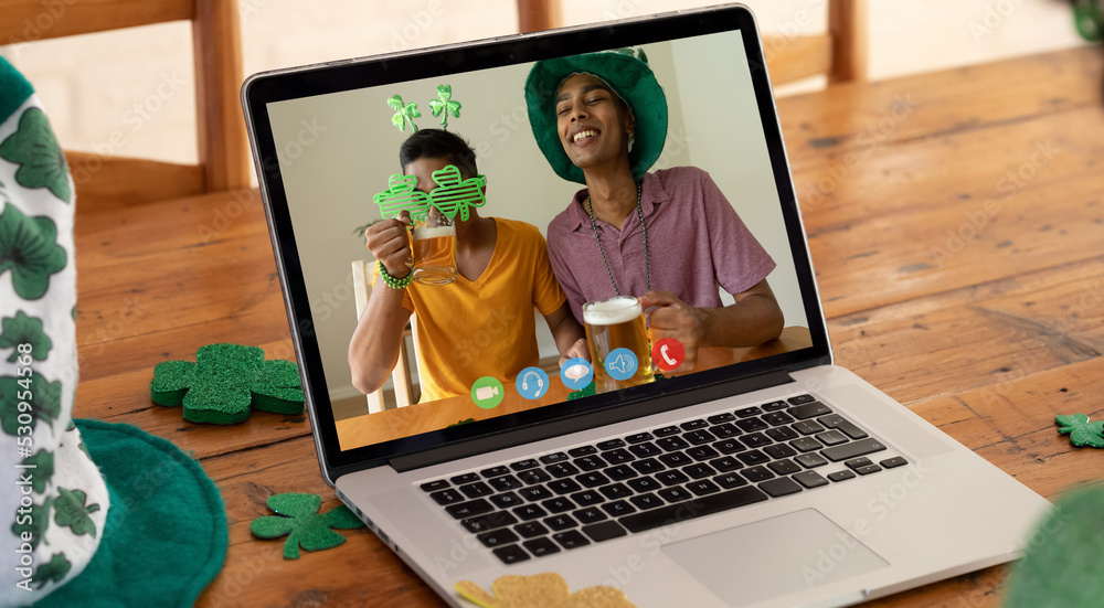 Webcam view of two african american men drinking beers on video call on laptop on wooden table