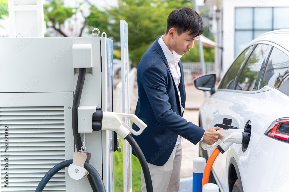 Asian man holding Electric Car Charging connect to Electric car on electric car charging station. Co