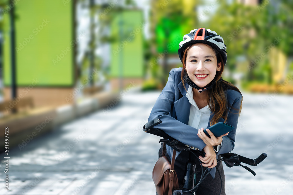 Young Asian businesswoman wearing helmet and standing on a city street with bicycle looking at phone