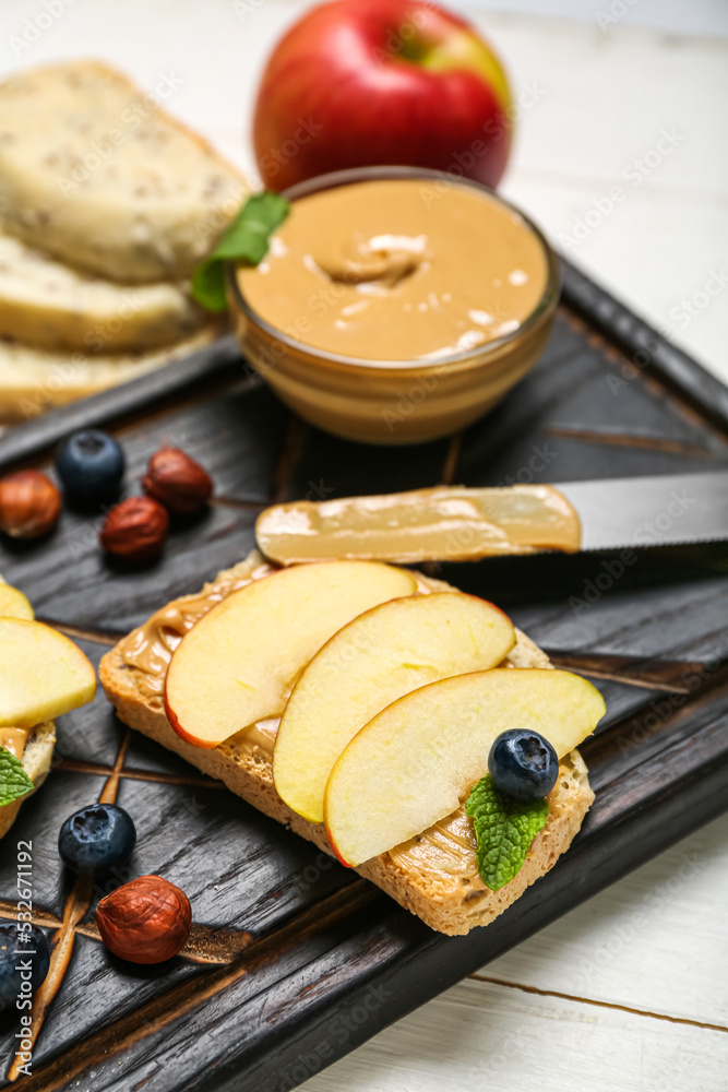 Wooden board of tasty sandwich with nut butter and apples on table, closeup