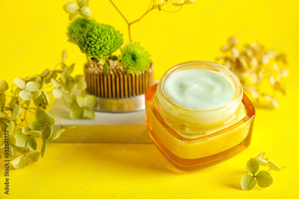 Jar of cream with ikebana on yellow background, closeup