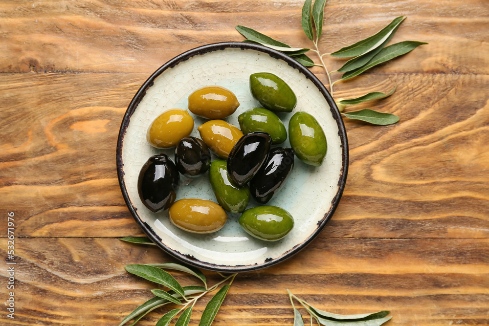 Plate with delicious olives on wooden background