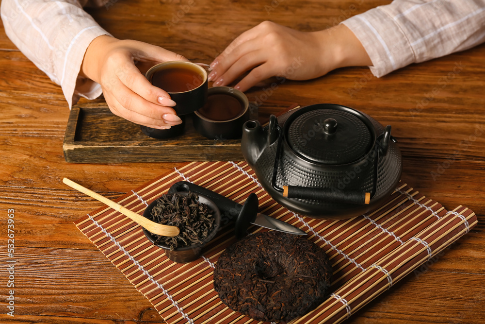 女性双手，木质背景上有一杯芳香的普洱茶