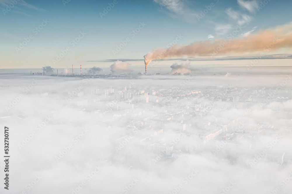 Foggy morning skyline view of downtown Płock with steaming refineries and industrial facilities in b