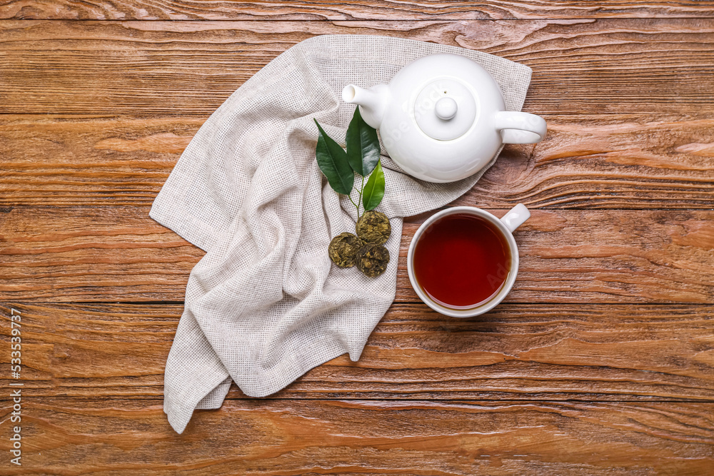 木质背景上的带有干压普洱茶、杯子和茶壶的餐巾