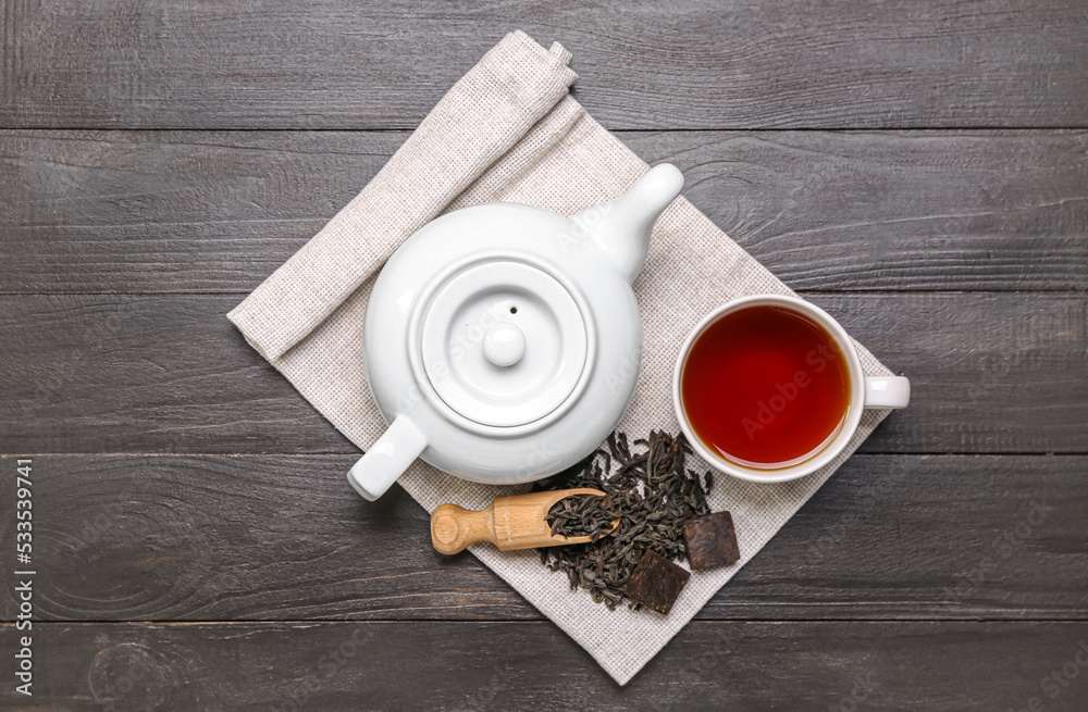 Napkin with scoop of dry puer tea, cup and teapot on dark wooden background