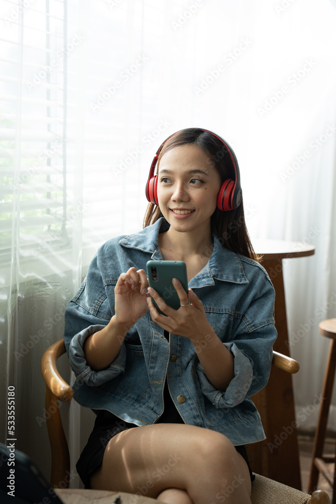 young woman using smartphone at table with laptop in coffee shop