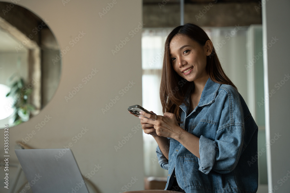 年轻的亚洲女人在咖啡店打电话，开心地笑着。