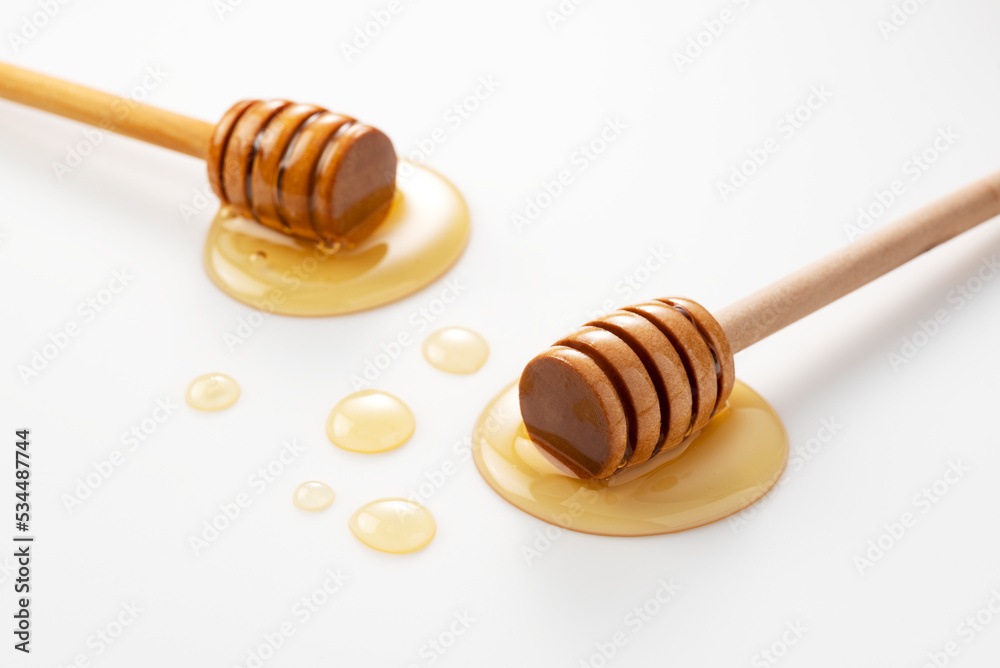 Wooden honey dipper with honey on white background.