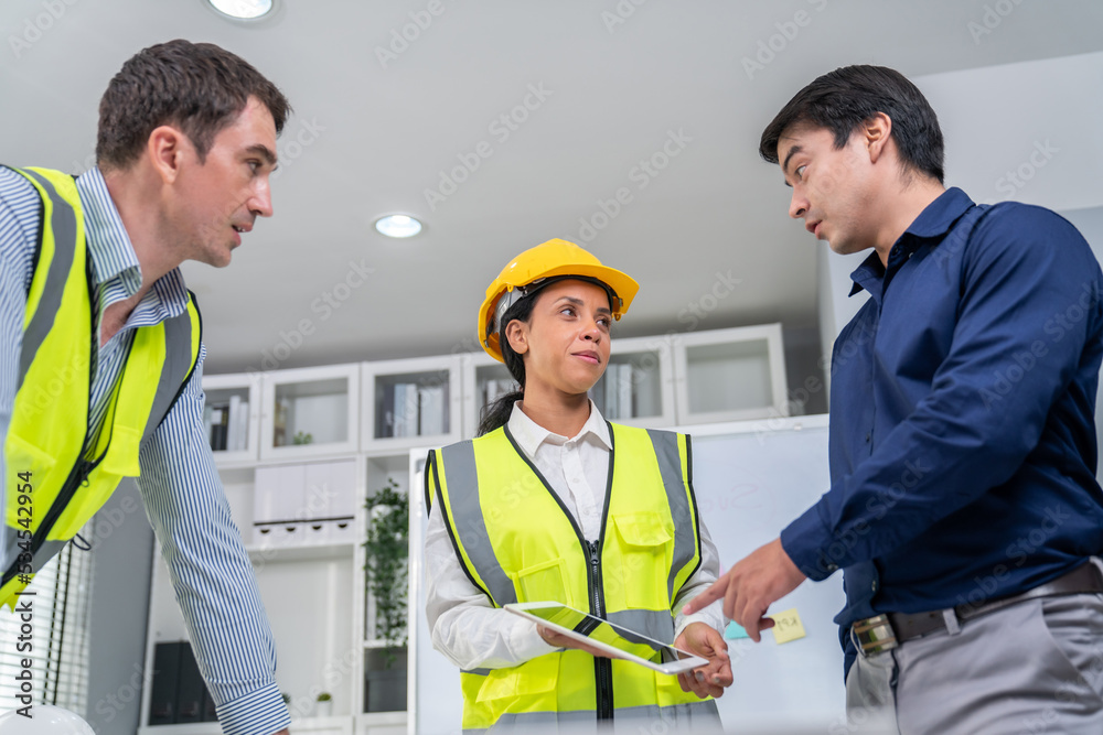 Engineers and competent employer discussing plans and blueprints together with tablet in the office.