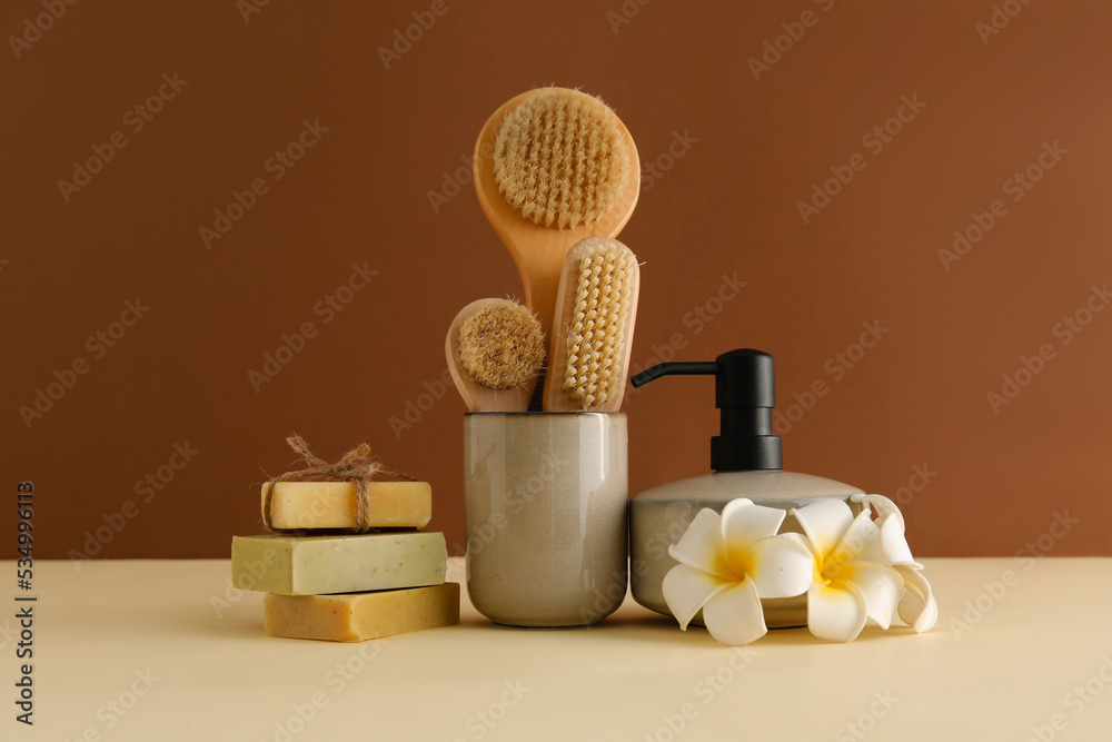 Bath accessories with flowers on table near brown wall