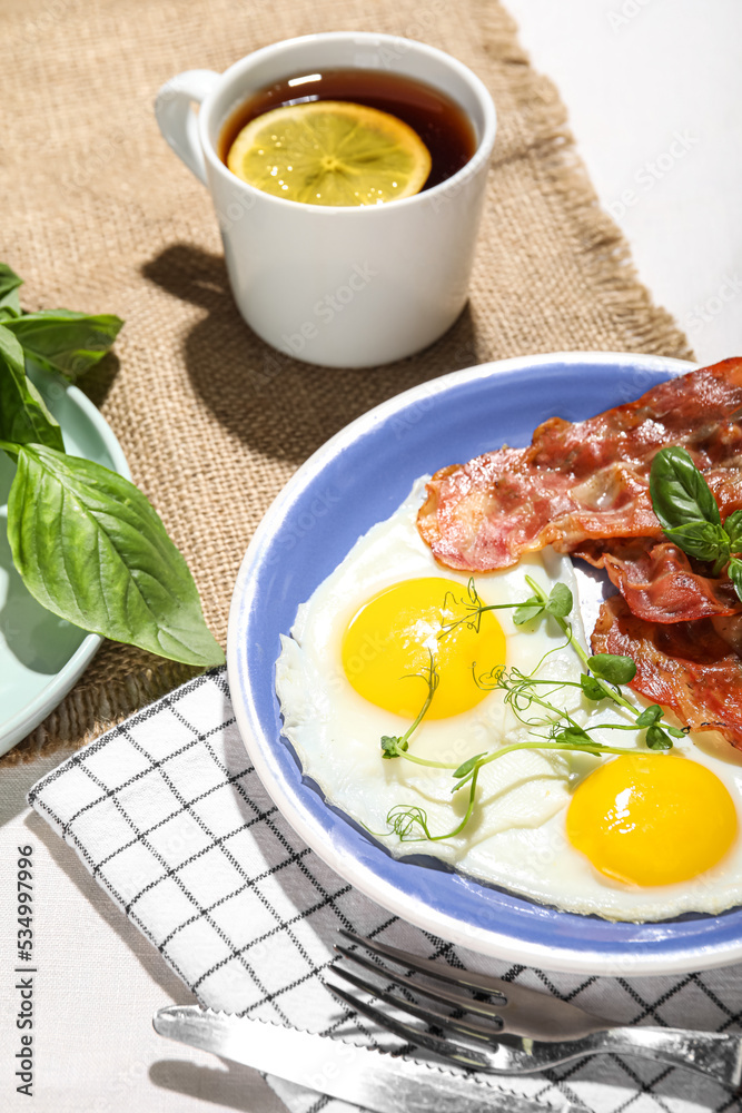 Plate with tasty fried eggs, bacon and cup of tea on table