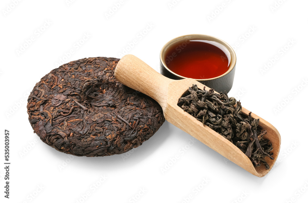 Scoop of dry puer tea and cup on white background