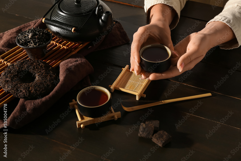 Female hands with cups of tasty puer tea on dark wooden table