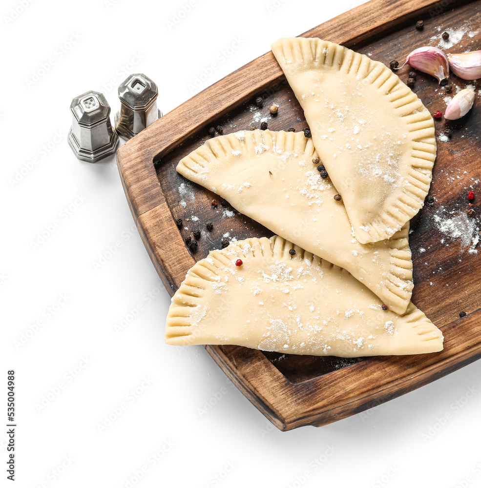 Board with raw chebureks and spices on white background