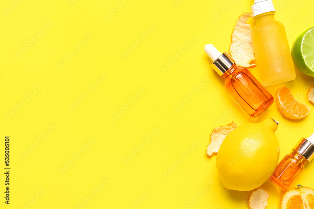 Composition with bottles of citrus serum and fruits on yellow background