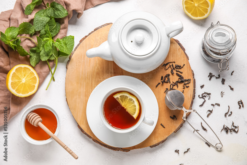 Board with cup of black tea, lemon, teapot and honey on white background