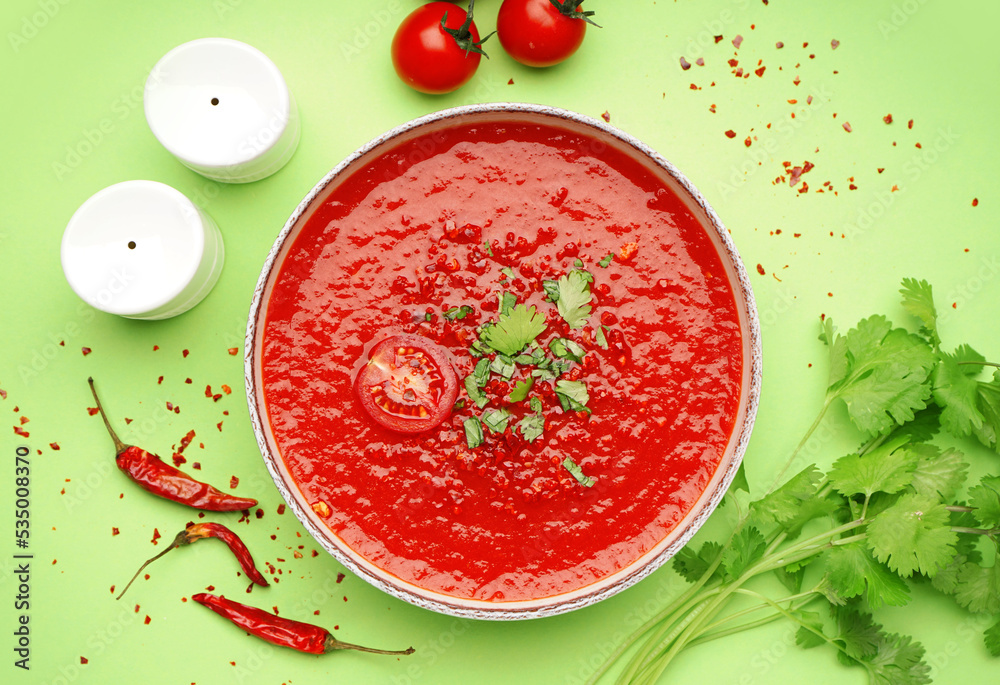 Bowl of tasty tomato soup and ingredients on green background