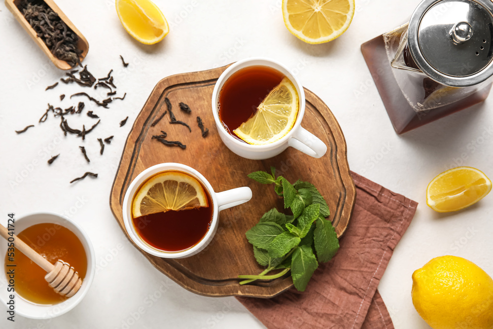 Board with cups of black tea, lemon, mint and honey on white background