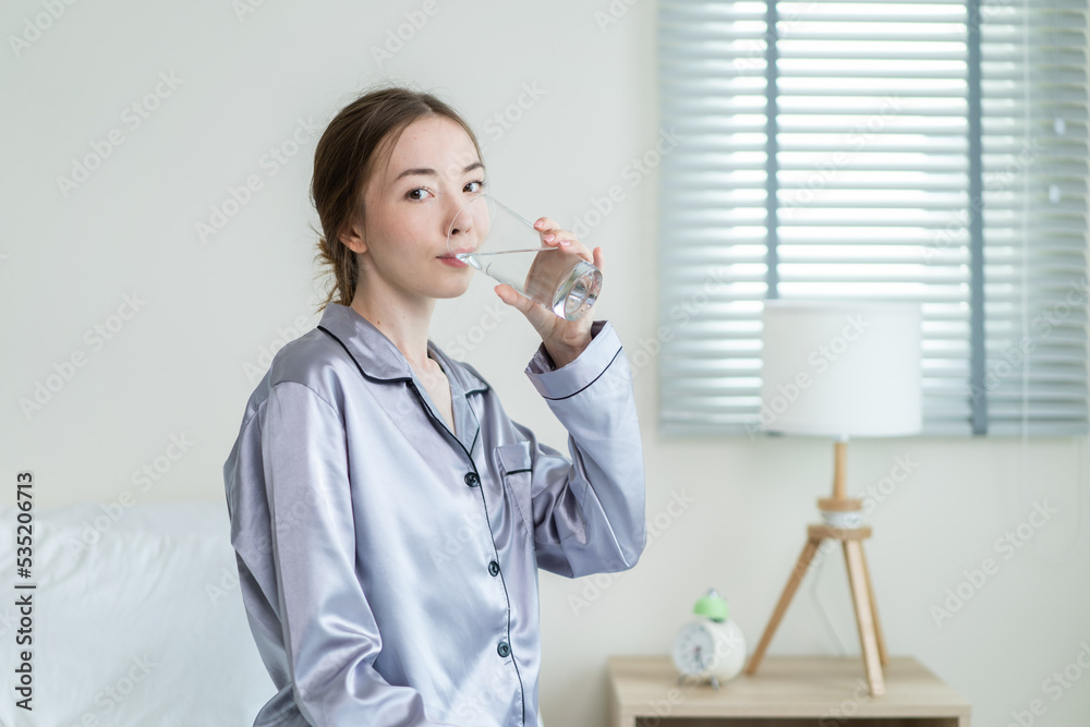 Cacasian女人坐在床上卧室喝水的肖像。