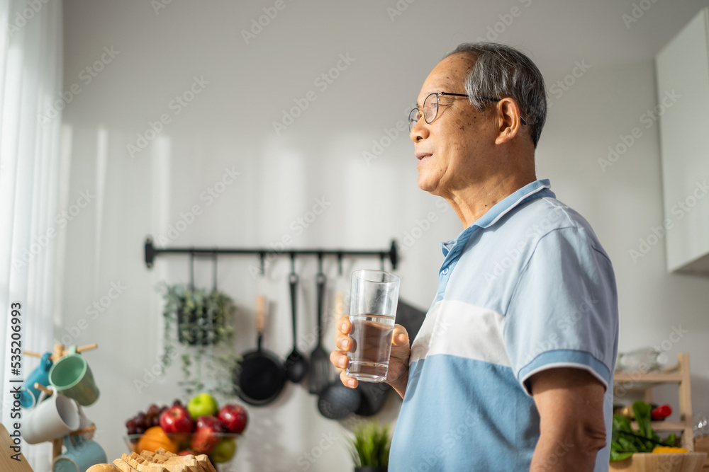 Asian senior mature male drinking a glass of water in kitchen at home. 