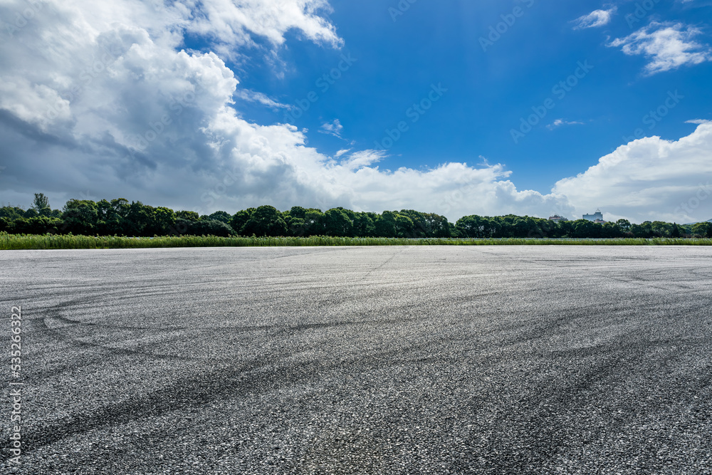 空旷的沥青赛道道路和天空云朵背景的绿色森林