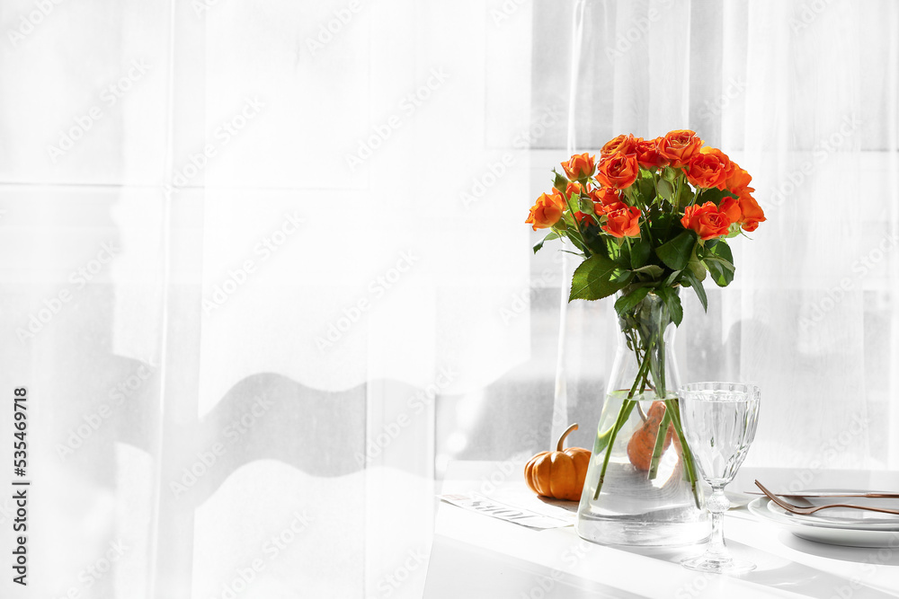 Vase with beautiful roses and glass of water on table in room