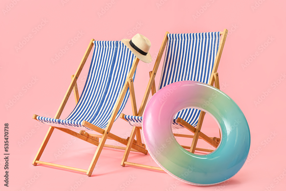 Beach deck chairs and inflatable ring on pink background