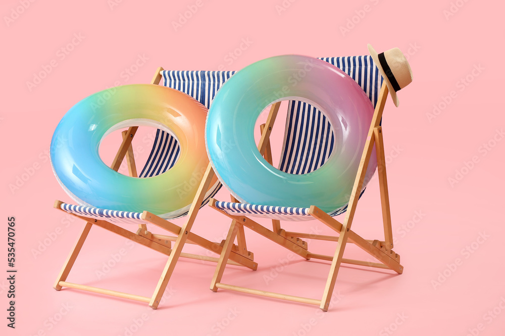 Beach deck chairs and inflatable rings on pink background