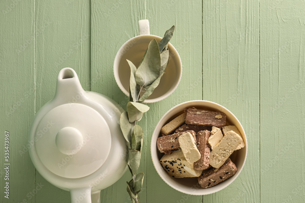 Bowl of tasty sesame halva and tea set on color wooden background