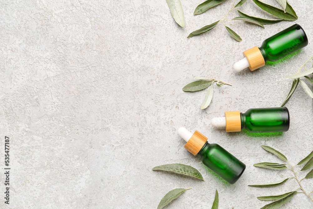 Composition with bottles of essential olive oil and plant leaves on light background