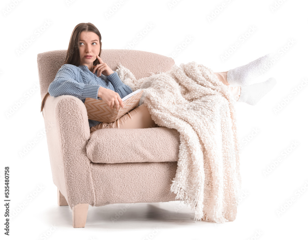 Thoughtful young woman with book and plaid sitting in armchair on white background