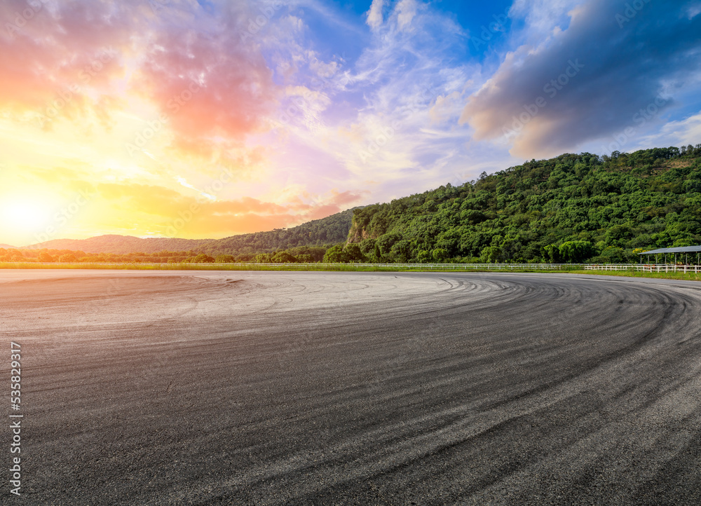 Empty asphalt race track road and green forest with sky clouds at sunset