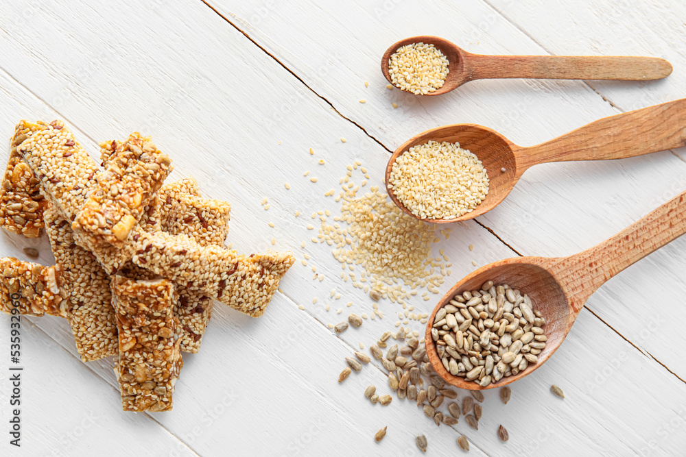 Heap of tasty sesame kozinaki and spoons with cereals on light wooden background