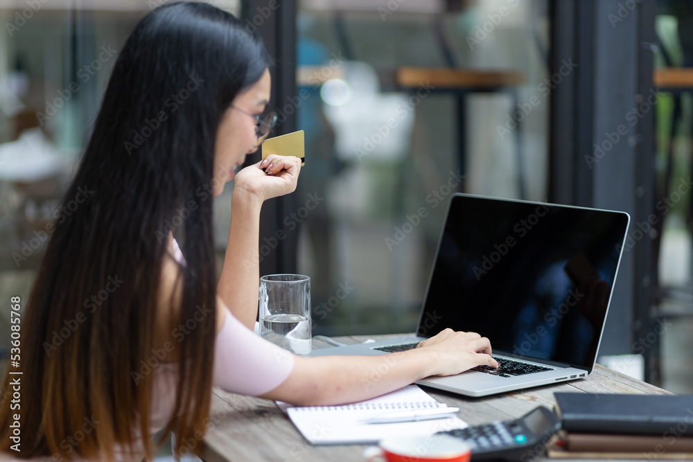 Attractive Asian woman holding a credit card and using a laptop is shopping online.