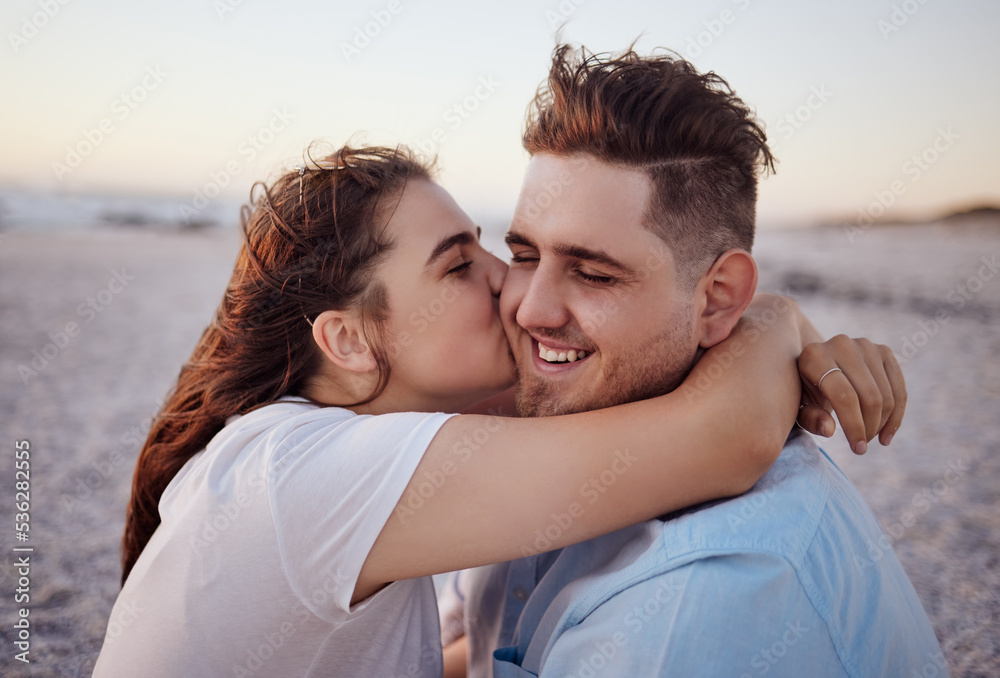 Love, couple and kiss on beach happy to celebrate relationship with sunset being relax, smile and on