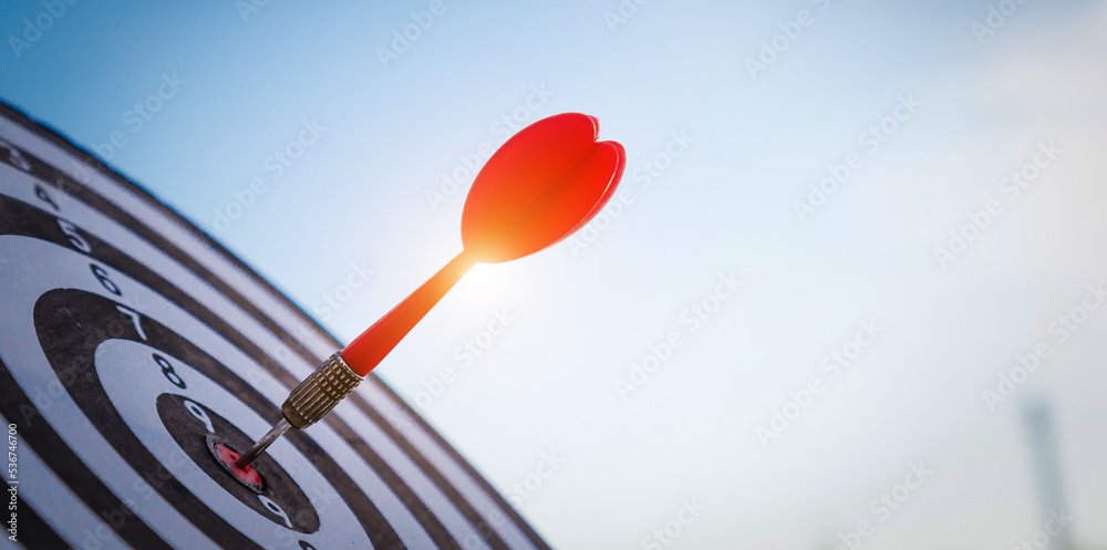 Close up shot red darts arrows in the target  of dartboard center on dark blue sky background. Busin