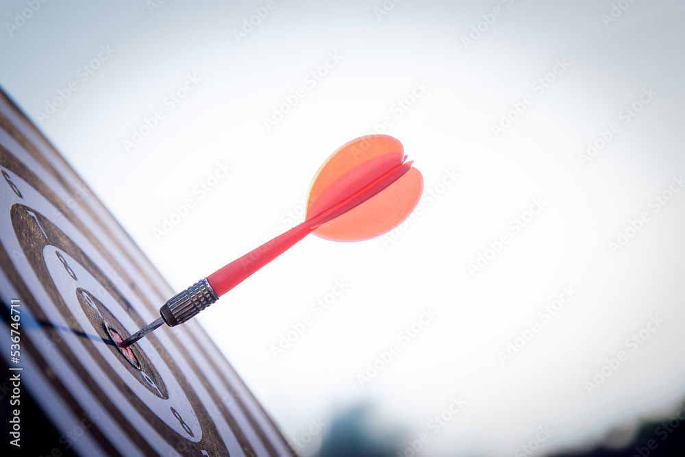 Close up shot red darts arrows in the target  of dartboard center on dark blue sky background. Busin