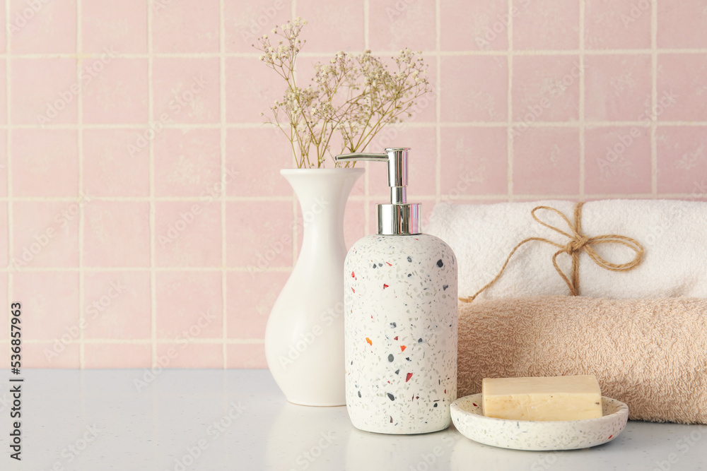 Bath accessories and vase with flowers on table near pink tile wall