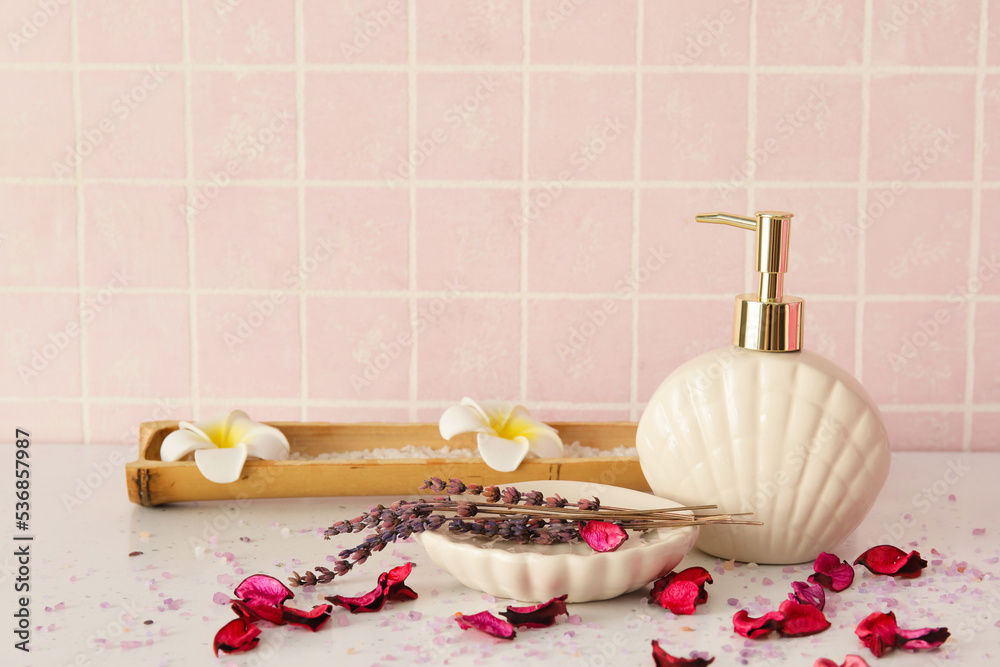 Bath accessories with flowers on table near pink tile wall