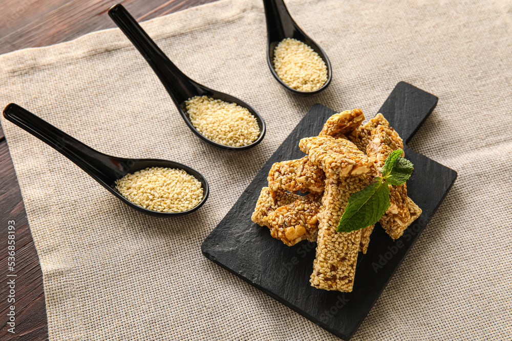 Board with tasty kozinaki and spoons of sesame seeds on table