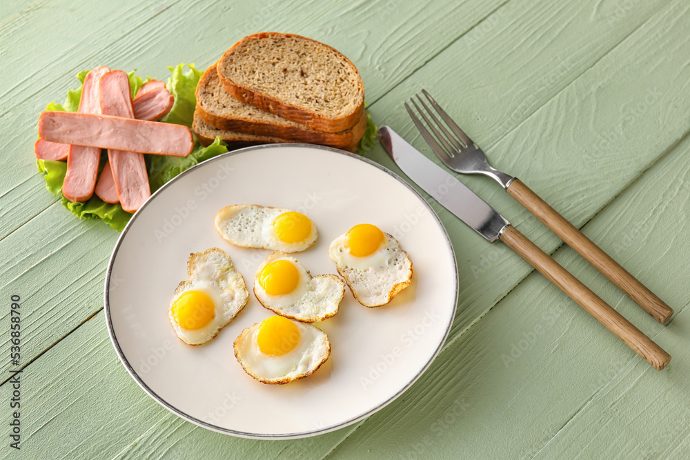 Plate with fried quail eggs, sausages and bread on color wooden background