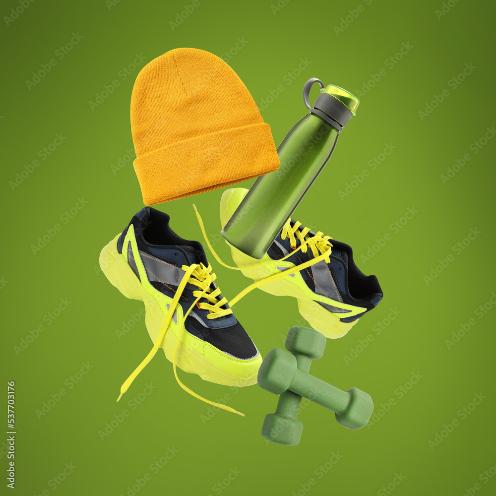 Flying sports shoes with dumbbells, hat and bottle of water on green background