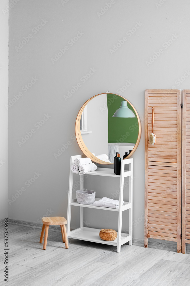 Shelving unit with bath supplies, mirror and folding screen near light wall