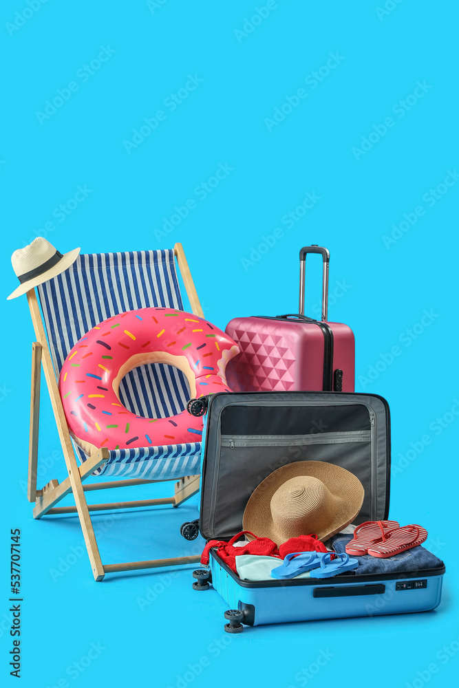 Deck chair, suitcases and beach accessories on light blue background