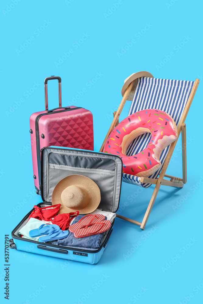 Deck chair, suitcases and beach accessories on light blue background