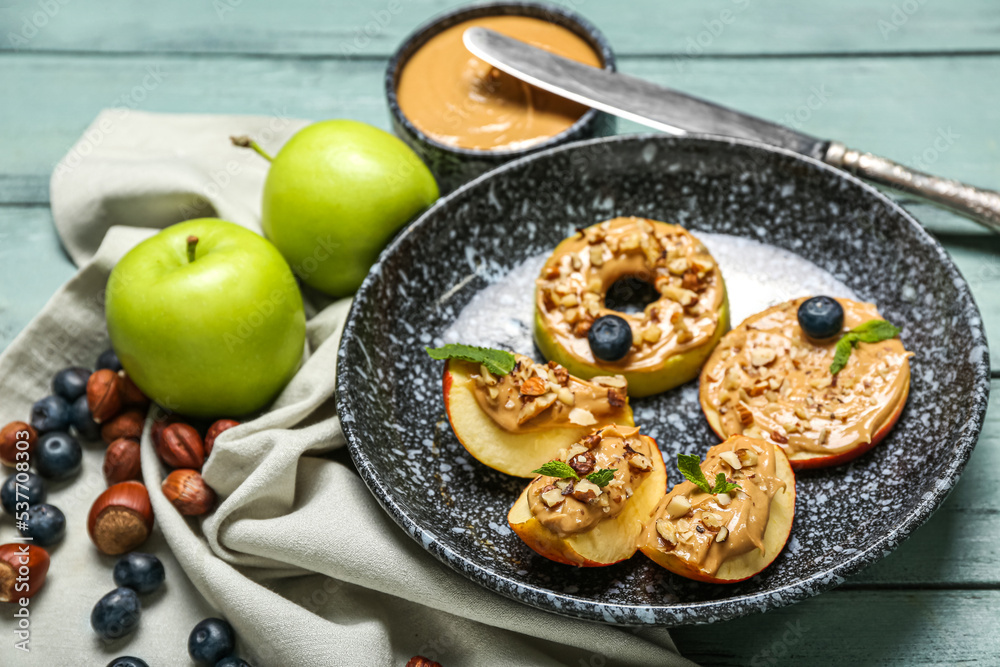 Plate of tasty apple wedges and rounds with nut butter on color wooden table