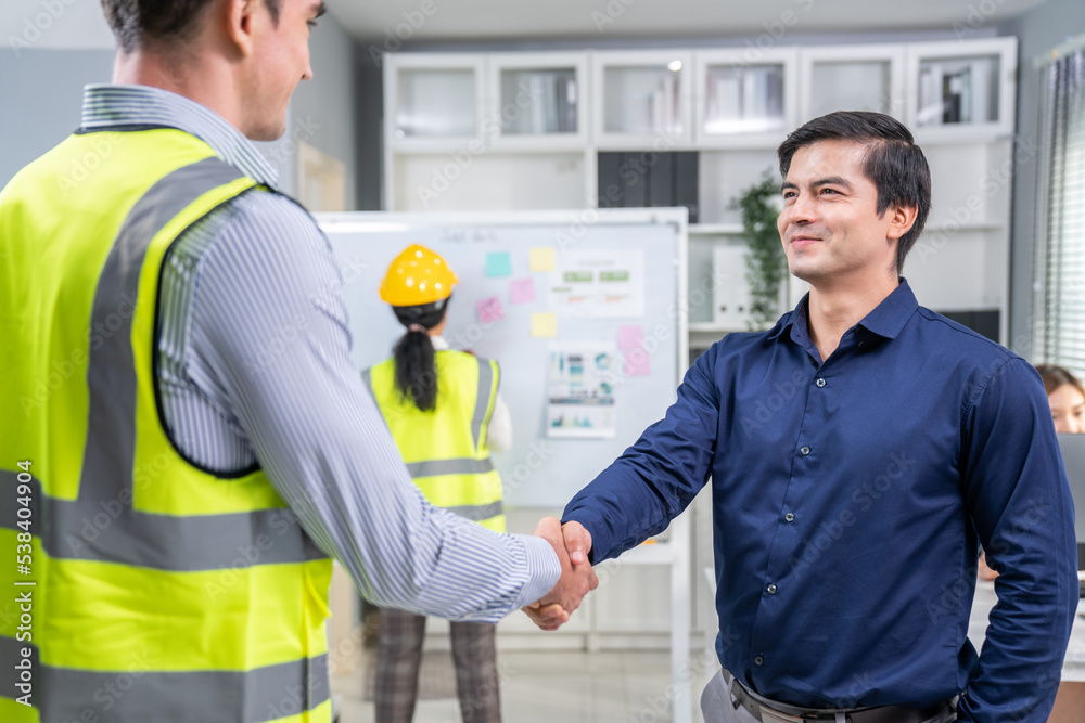 An engineer with a protective vest handshake with an investor in his office. Following a successful 