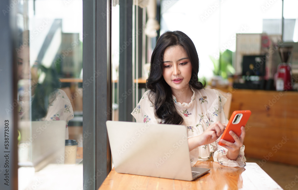 一位年轻女士在咖啡馆的桌子上用智能手机和笔记本电脑。